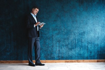 Happy mature businessman working with modern tablet isolated on dark blue background.