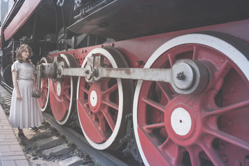 Fototapeta premium Woman stands near the wheels of the locomotive. Girl looks at the big wheel train. Vintage steam train stands on the tracks