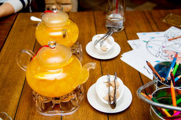 2 teaspoons of sea buckthorn and orange tea stand on tea burners, white and brown sugar on white saucers next to a wooden table in a cafe or restaurant