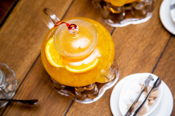 teaspoon of sea buckthorn and orange tea stand on tea burners, white and brown sugar on white saucers next to a wooden table in a cafe or restaurant