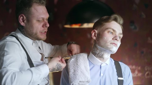 Tattooed barber shaves his tattooed client with straight razor, barber shop in 30's mafia style, shaving salon, 4k UHD 60p Prores HQ 422
