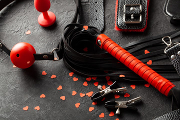 BDSM sex toys for adults. Small red hearts on black background whip, gag, handcuffs and leather...