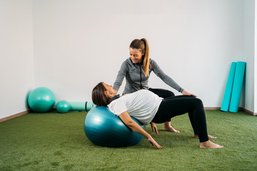 Pregnant woman doing fitness ball and pilates exercise with coach. Happy future mother preparing...