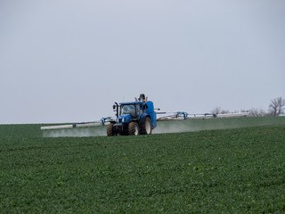A blue tractor sprays pesticides on a green field. Blue tractor on field. 