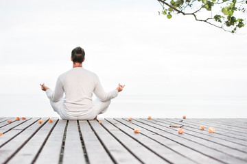Man in white clothes meditating yoga on wooden pier