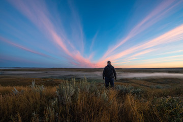 A Man Stands Watching Watching The Sunrise Colour Over The Frenchman River Valley In Grasslands National Park; Saskatchewan, Canada