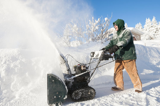 A Man Happily Using His Snowblower In Front Of His House; Alaska, United States Of America