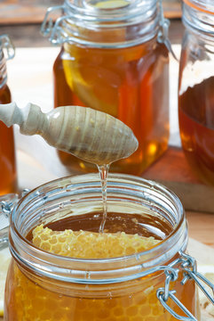 A wooden dipper dripping above a jar of honey with honeycomb