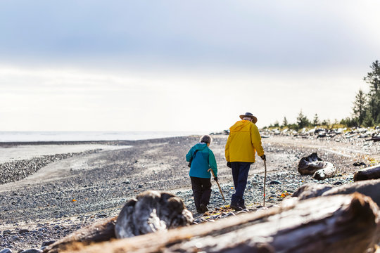 A senior couple hiking with walking sticks on the beach along the coast, Meadow Mist Campground, Graham Island; Tlell, Haida Gwaii, British Columbia, Canada
