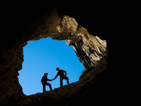 A young couple climbing in the mouth of a cave, holding hands for support; Fernie, British Columbia, Canada