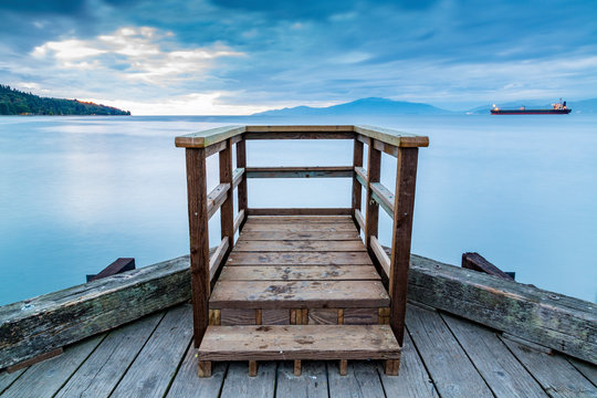 A wooden viewing platform at the end of a dock looks out to a ship on the tranquil ocean; Vancouver, British Columbia, Canada