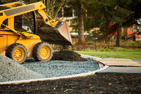 Small front end loader moving and placing gravel in a park area for new home construction; Langley, British Columbia, Canada