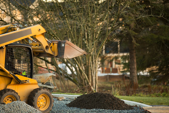 Small front end loader moving and placing gravel in a park area for new home construction; Langley, British Columbia, Canada