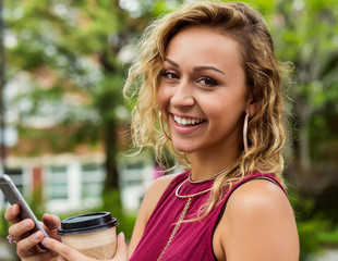 A beautiful young woman texting on her smart phone on a university campus and pausing to look at the camera; Edmonton, Alberta, Canada