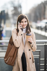 Young brunette walking street enjoying a coffee and talking over the phone