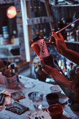 Process of creating a designer coffee cup for a customer. Art studio with necessary tools at background.