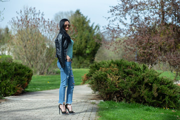 Brunette in sunglasses and black is standing and enjoying the sun in the park