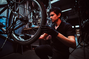 Fototapeta na wymiar Handsome diligent master is fixing bicycle's wheel at his workplace.