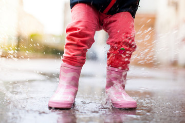 Kind hüpft mit rosa Gummistiefeln in Wasserpfütze. Child jumps with pink rubber boots in puddle.