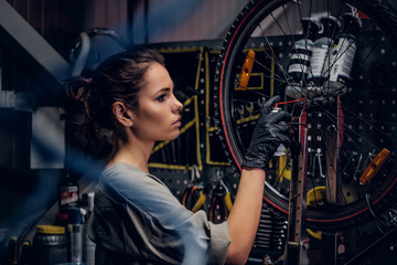 Obraz na płótnie Canvas Young beautiful woman is repairing bicycle at busy workshop between pneumatic wires.