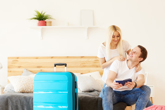 Smiling couple of tourists with passports and tickets in hotel room keep a suitcase with luggage. Waiting for a flight from the airport. The girl hugs the guy, they are going on a honeymoon trip