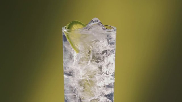 Soda water or a Sprite spinning glass with lime, slow motion bubbles, ice cold.