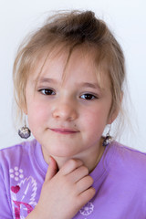 Vertical closeup of beautiful little girl in pale purple top trying on adult pendant earrings