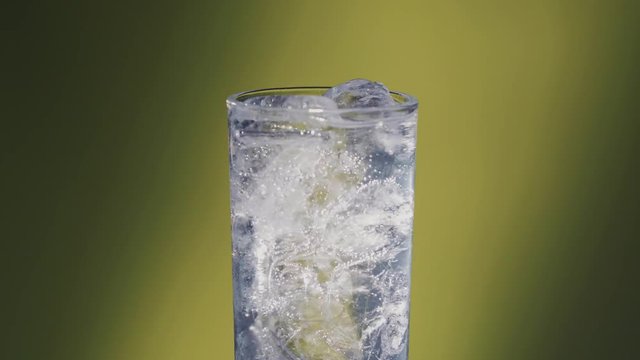 Lights turn on a Soda water or a Sprite spinning glass, slow motion bubbles, ice cold. 3 takes, yellow atmosphere.