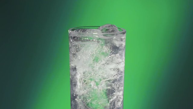 Lights turn on a Soda water or a Sprite spinning glass, slow motion bubbles, ice cold. 3 takes, green atmosphere.