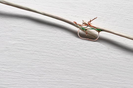 Broken cable against a white wall. Copper wires are twisted by hand and not insulated.