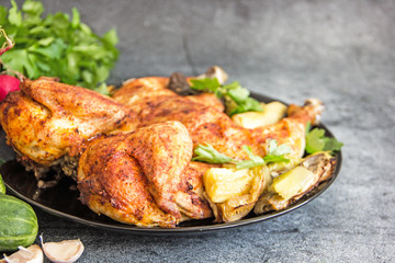 Chicken tobacco national dish of Georgian cuisine. Baked chicken with garlic and grilled vegetables on a black plate on a stone background, next to fresh greens and vegetables.  Copy space