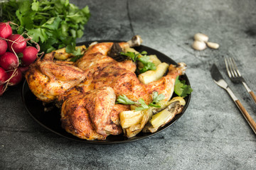Chicken tobacco national dish of Georgian cuisine. Baked chicken with garlic and grilled vegetables on a black plate on a stone background, next to fresh greens and vegetables.  Copy space