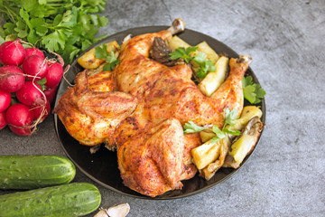 Chicken tobacco national dish of Georgian cuisine. Baked chicken with garlic and grilled vegetables on a black plate on a stone background, next to fresh greens and vegetables.  Copy space