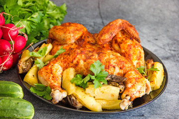 Chicken tobacco national dish of Georgian cuisine. Baked chicken with garlic and grilled vegetables on a black plate on a stone background, next to fresh greens and vegetables.  Copy space