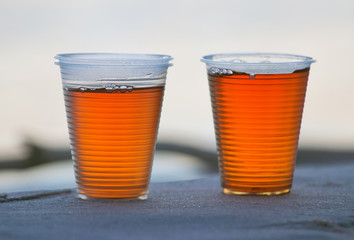Two plastic cups of tea on sand, close-up