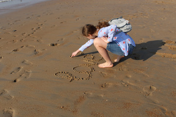 The girl writes the word "Love" and nd a symbol of heart on the wet sand at sunset.