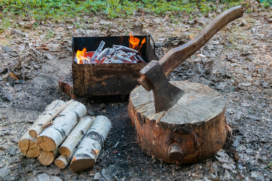 The axe in the log and wood against grill fire for cooking BBQ meat. Outdoor picnic