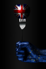 A hand with a drawn EU flag holds a fork, on which is a ball with a drawn Great Britain flag, a...