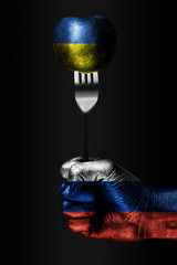 A hand with a drawn Russia flag holds a fork, on which is a ball with a drawn Ukraine flag, a sign...