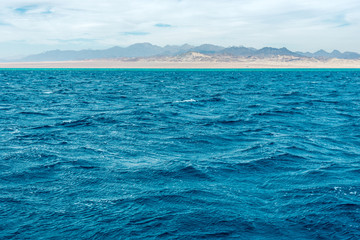 Seascape, view of the blue sea with high bald mountains in the background
