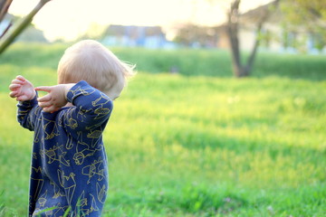 Toddler blond boy on green bright grass on a sunny day, selective focus.