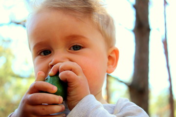 A boy of European appearance is eating with his hands a fresh clean cucumber on the street close-up.