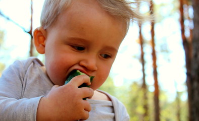 A boy of European appearance is eating with his hands a fresh clean cucumber on the street close-up.