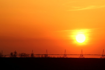 Sunset orange sky over the field with frigates for watering in the spring evening away.