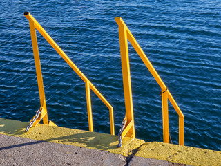 Yellow stairs and handrails on the docks - deep blue sea in the background