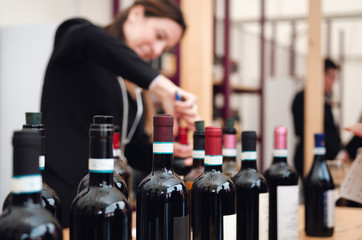 Tasting experience with bottles and an out of focus  female sommelier uncorking a bottle of red...