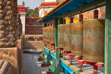 Row of mani prayer wheels of Putuo Zongcheng Buddhist temple, one of the Eight Outlying temples in Chengde, Heibei, China. Unesco World Heritage Site. Monks and people praying in background.