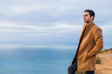 The guy holds his hands in his pockets in a beige coat standing