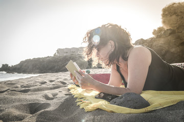 Beautiful girl relaxing at the beach reading a book. Portrait of a woman lying on a towel in a...