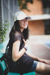 portrait of asian teenager wearing white cap sitting outdoor and  looking with eye contact to camera